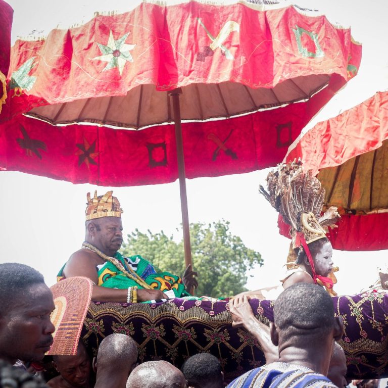 A chief in a palanquin under red state umbrellas