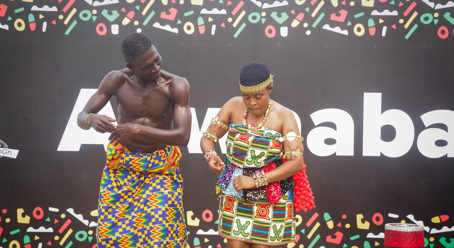 A man and woman dancing adowa in front of an Akwaaba banner