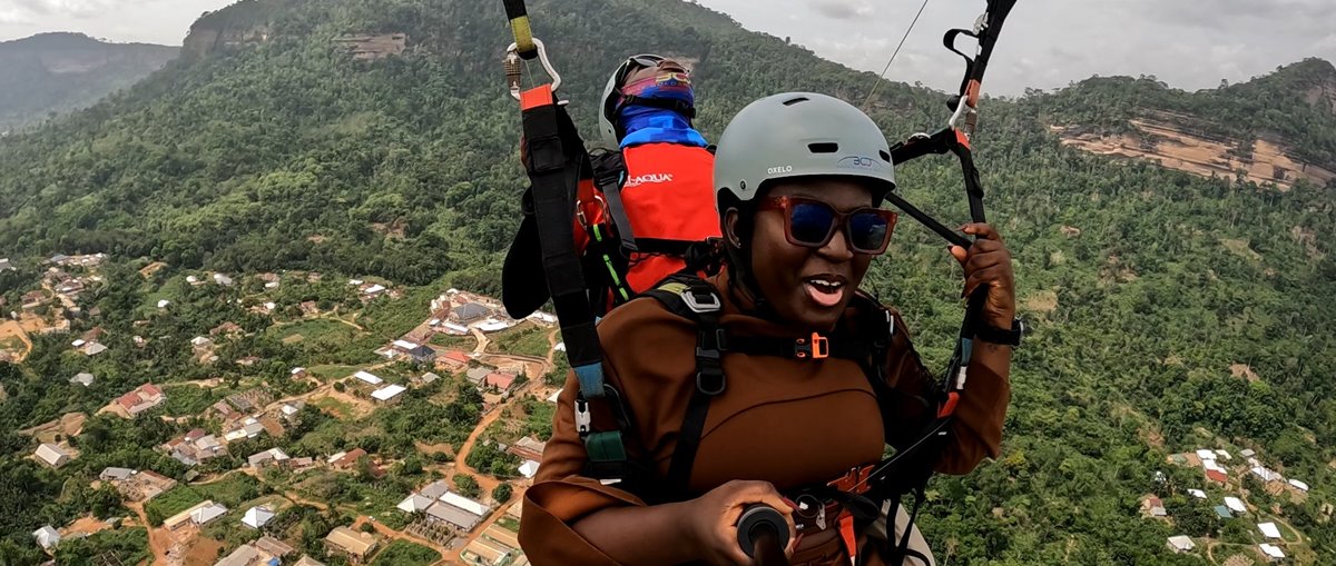 A tandem paraglider passing the forested Kwahu escarpment